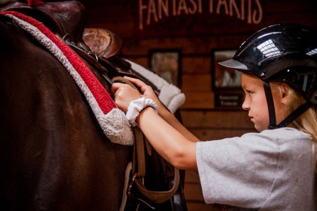 girl tacking horse at Fantasy Farms in Turner Oregon with helmet on and saddle